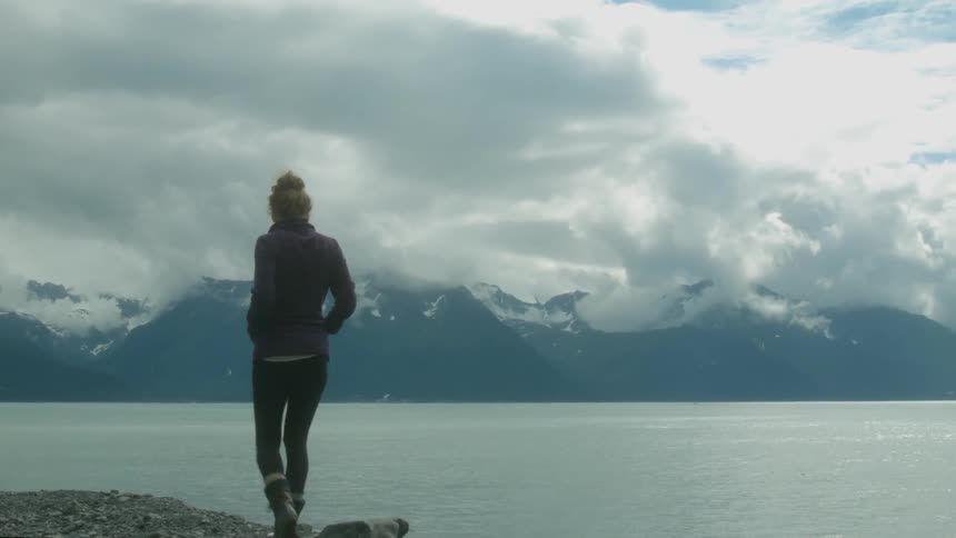 A woman is walking along the water on a cloudy day