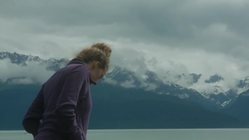 A woman in a jacket walks on the shore