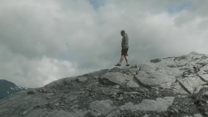 A man is walking over the mountain on a cloudy day