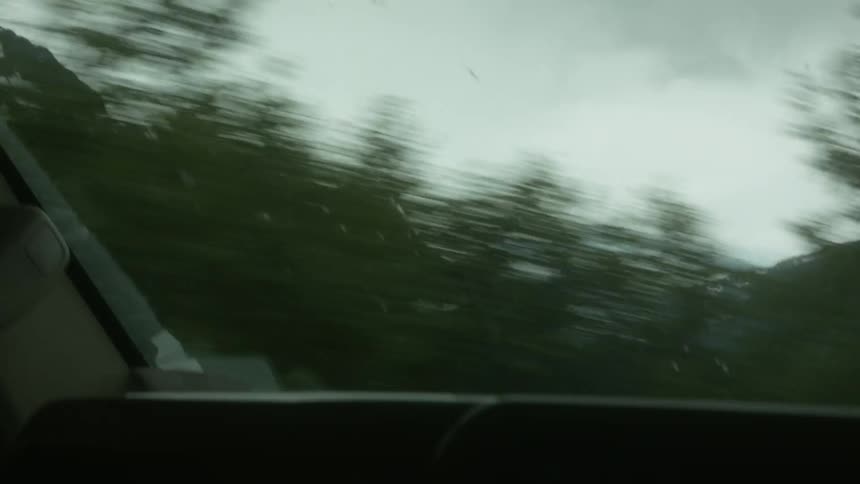A car is driving along a country side road with mountains in the distance
