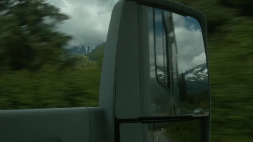 The rearview mirror shows the forest as the vehicle travels