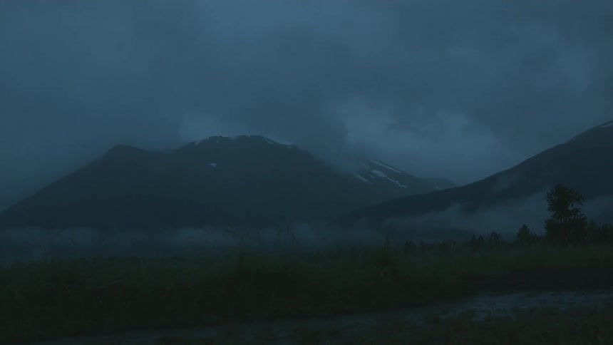 Very low clouds hover over a field and the mountains