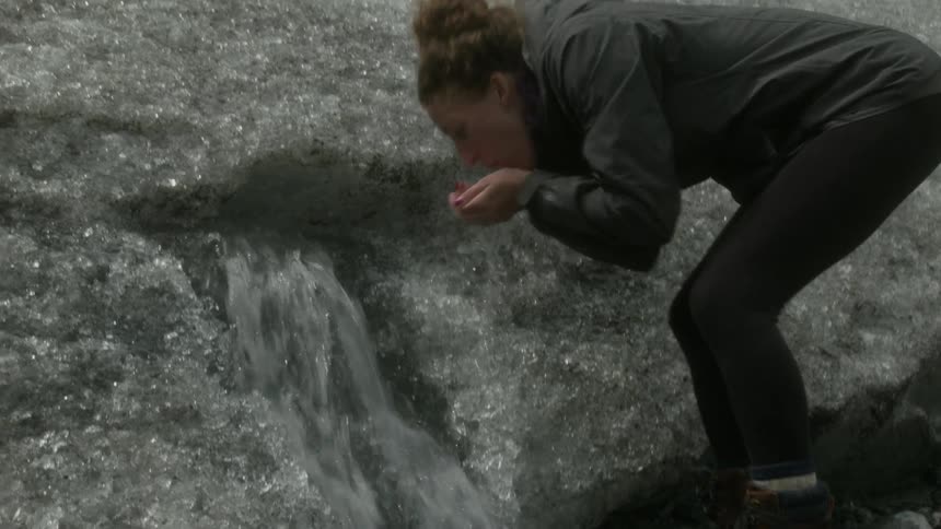 A woman drinks some water from a melting iceberg
