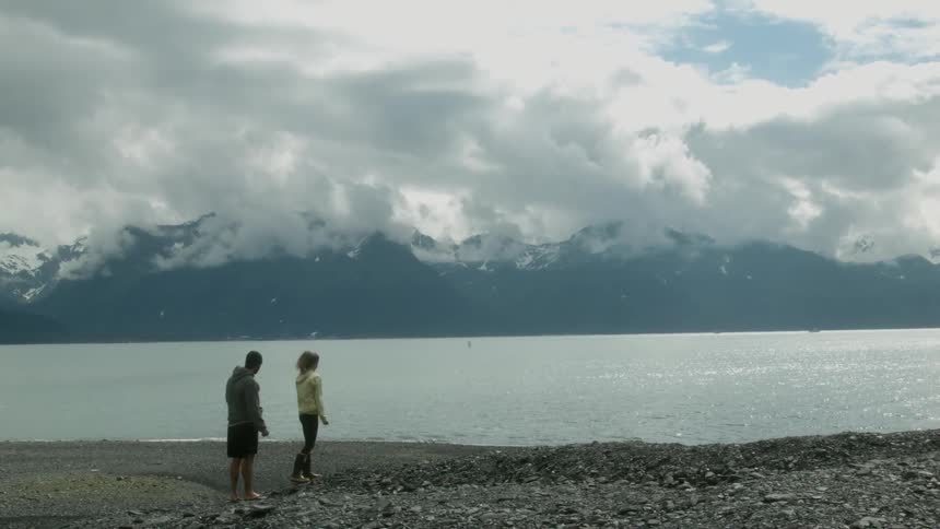 Two people are picking up rocks and skipping them in the lake