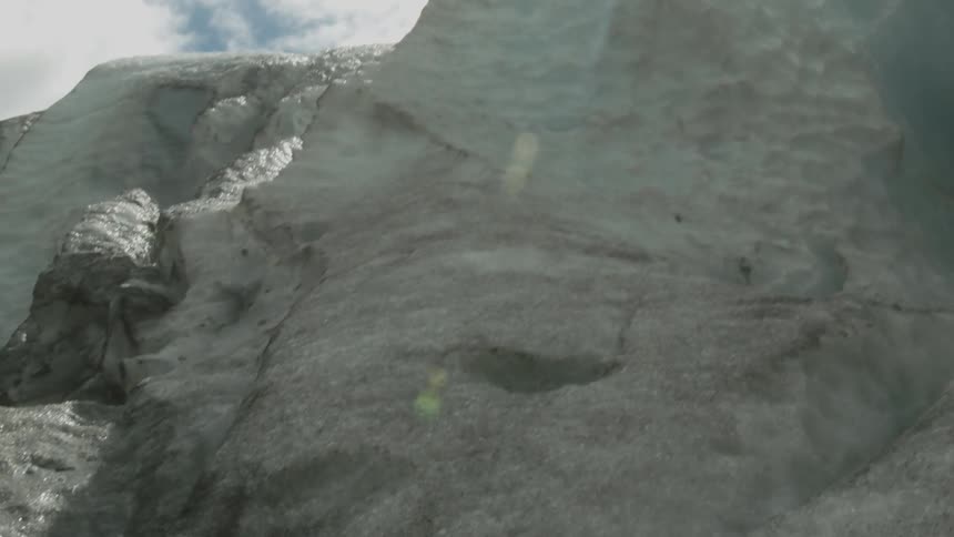 The tall wall of ice has the sun shining over the edge