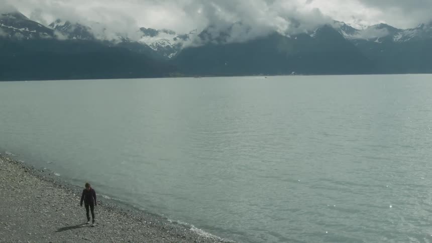 A woman is trying to skip pebbles on a mountain lake during the day