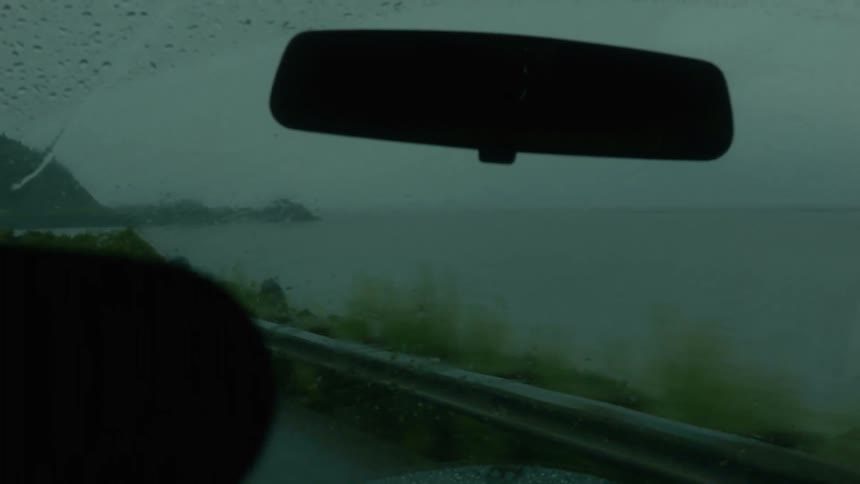 A car drives through the rain over a bridge