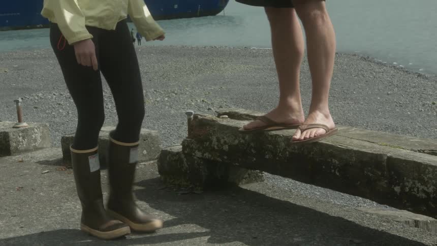 A woman walks over to a man standing on a bench and steps up