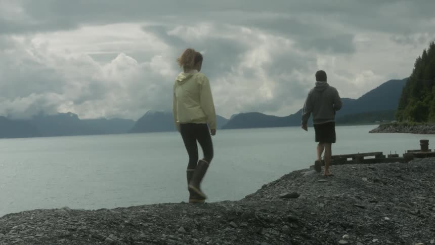Man and woman walk next to mountain lake
