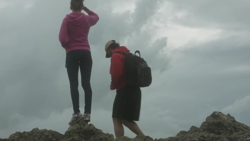 A woman stands on the rocks as a man climbs down
