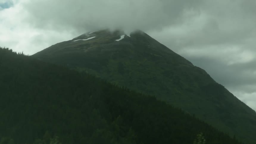 Clouds hover over a mountain peak off a highway during the day