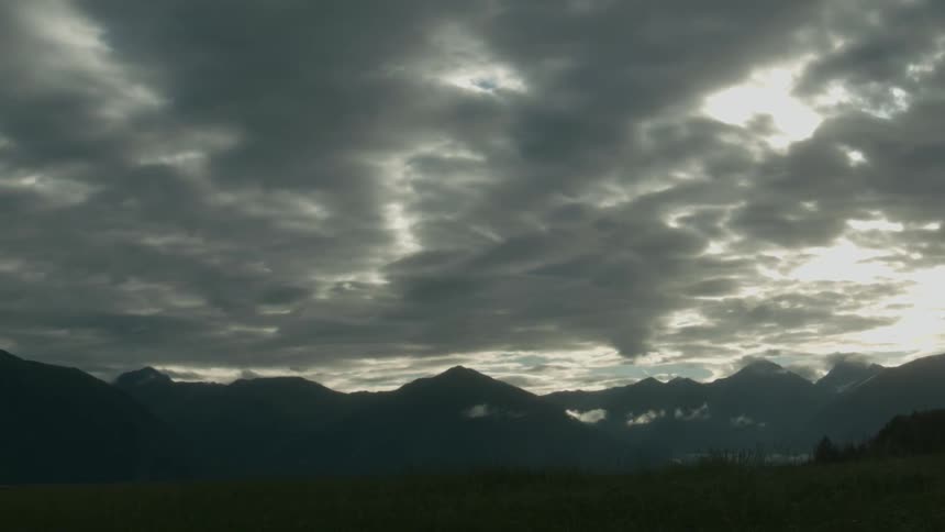 The sun is setting behind the mountains on a cloudy day