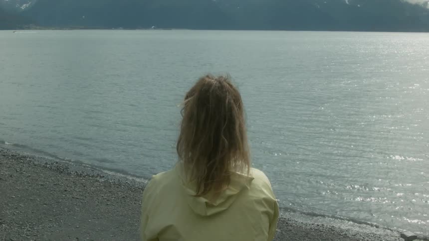 A woman is sitting on a pier that over looks a large calm lake