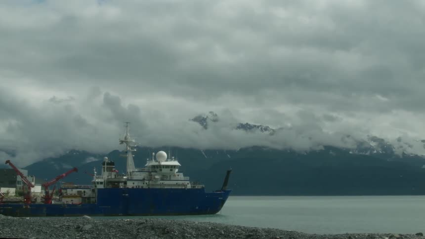 A commercial boat sits in a harbor near mountains covered by low clouds