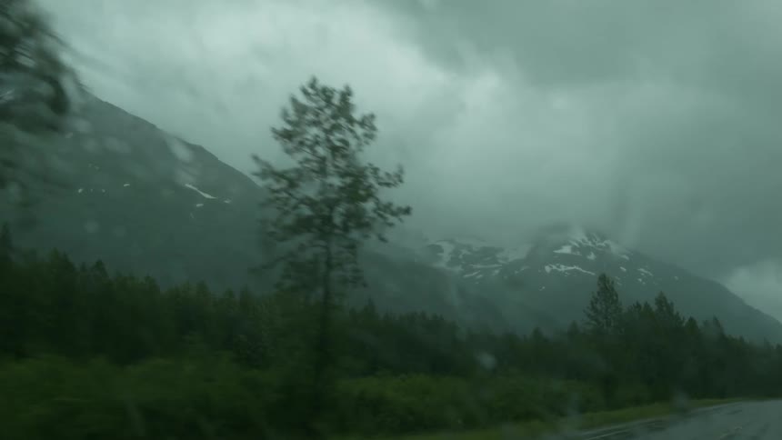A rainy foggy road with mountains on each side