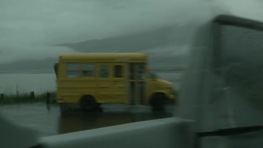 A vehicle passes by a small yellow bus on a rainy road