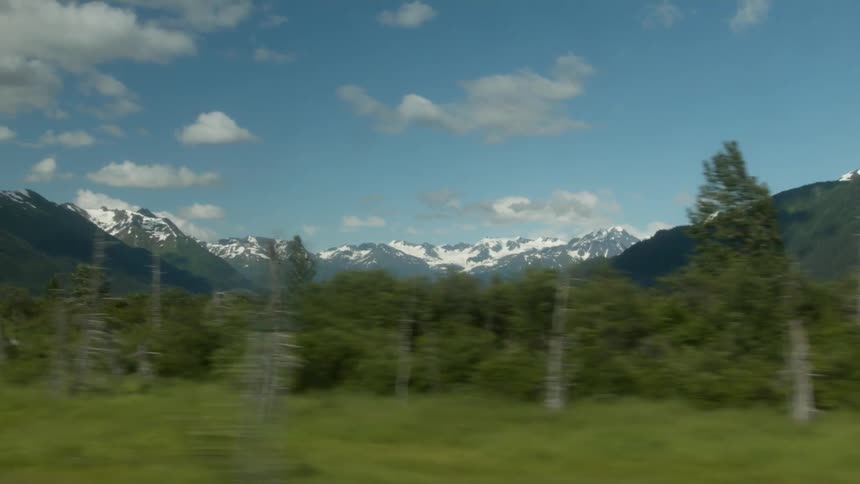 There is a long green field before the snow covered mountain