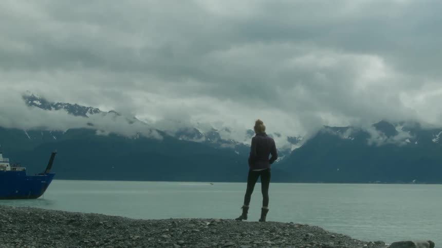 A woman is standing near the shore by a boat