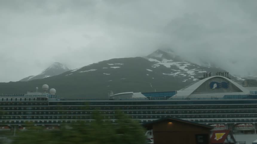 A cruise ship docked with a snow capped mountain behind it