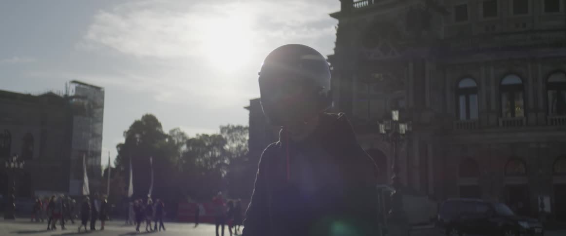 A man stands wearing a motorcycle helmet as others pass by
