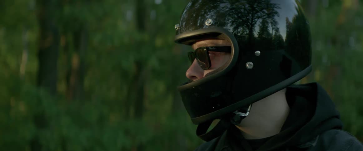 Man wears motorcycle helmet in forested area