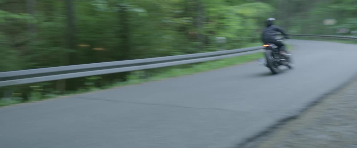 Person rides motorcycle down a country road surrounded by trees