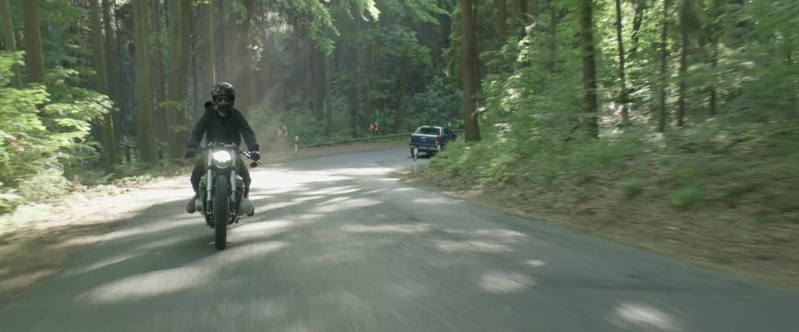 A man is riding a motorcycle on a road through a forest