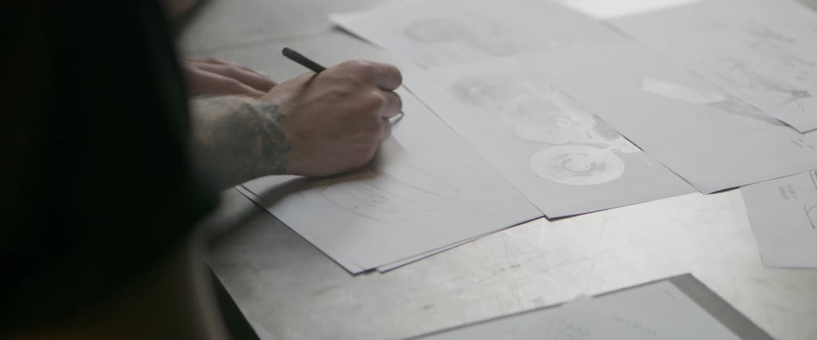 A man is sketching on a piece of paper on a drafting table in a garage