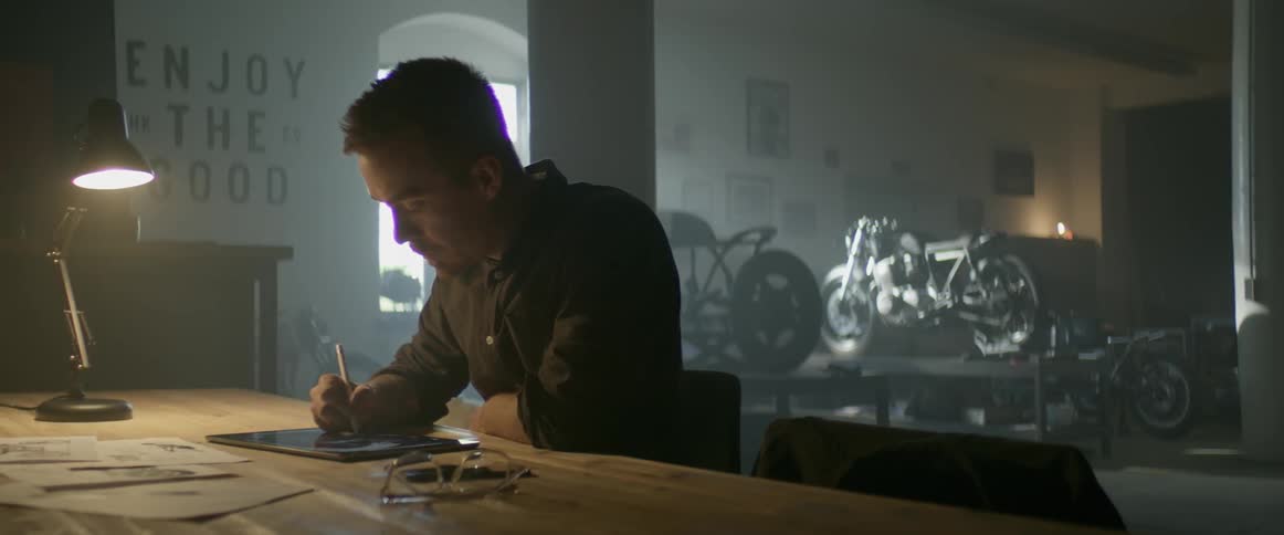 A man is sitting at his work bench drawing on his tablet pc
