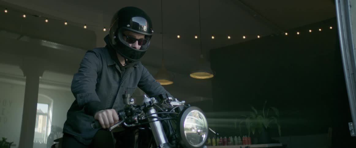 A motorcyclist puts sunglasses on and pulls out of a garage