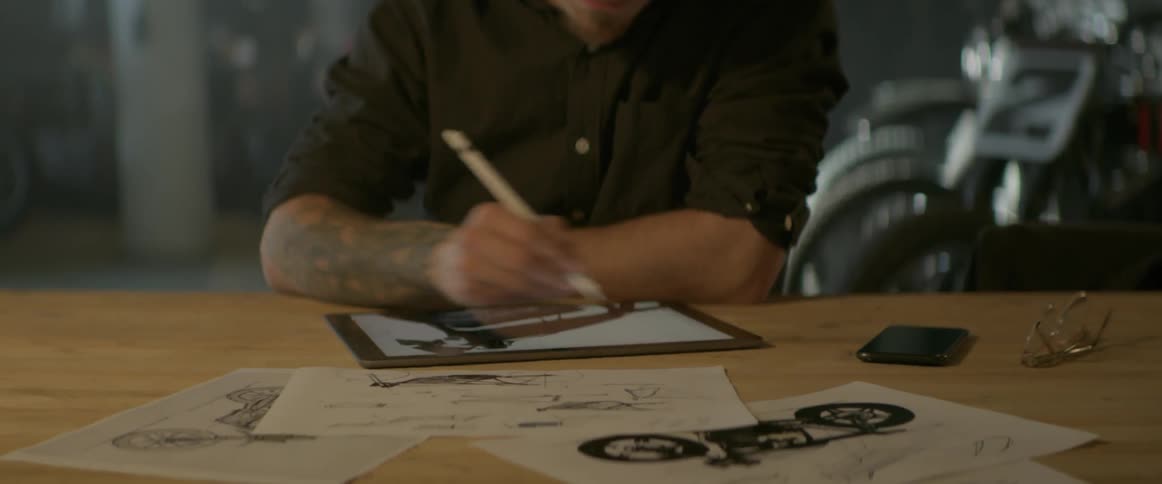 A man draws on a computer tablet as he sits at a table in a garage