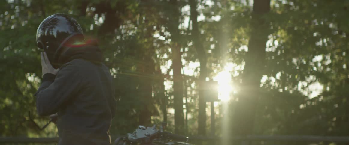 A man hikes down a trail holding his helmet