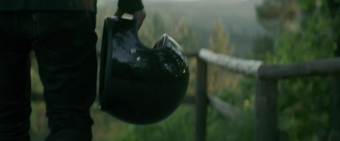 A person holding a helmet walks past a fence