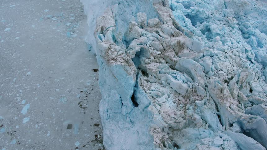 Ice and debris float in the ocean at the base of a glacier