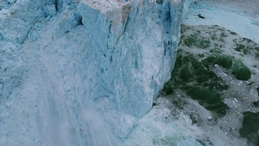 A chunk of ice falls off an iceberg into the water