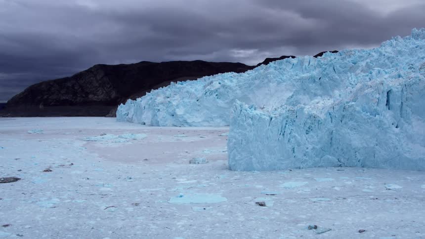 Ice and debris float in the ocean at the base of a glacier on a stormy day