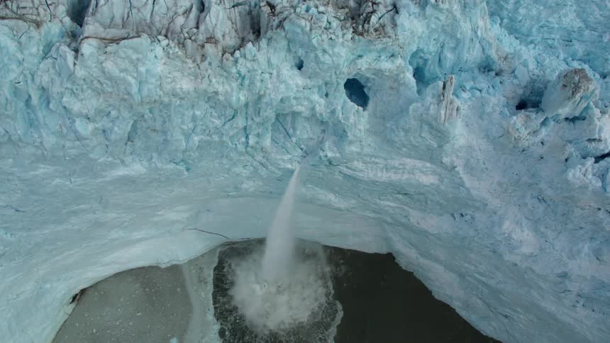 Snow and ice calves off a glacier and splashes in the ocean