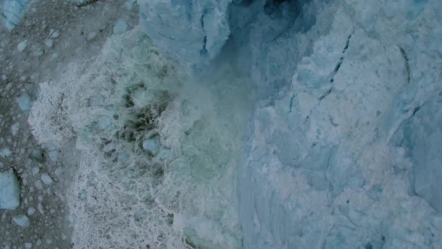 Snow and ice calves off a glacier and splashes in the ocean
