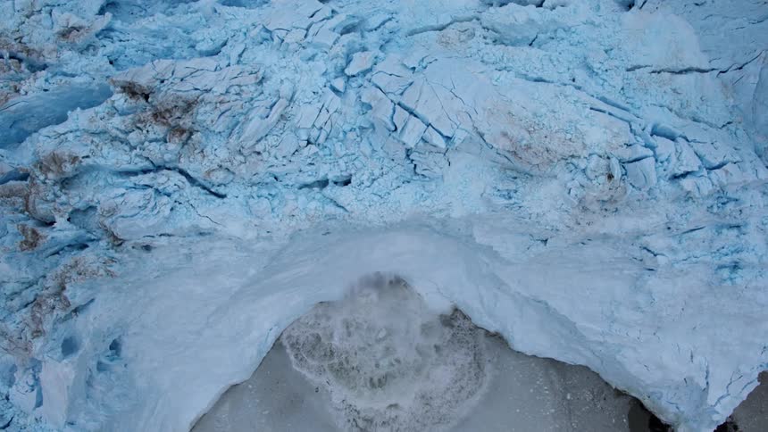 Snow and ice calves off a glacier and splashes in the ocean