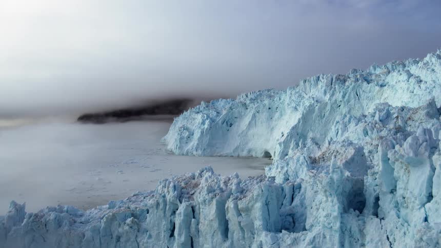 A large island of ice is blue near the shore
