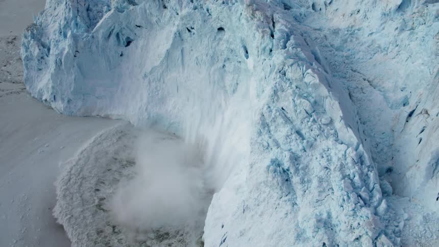 Snow and ice calves off a glacier and crashes into the ocean