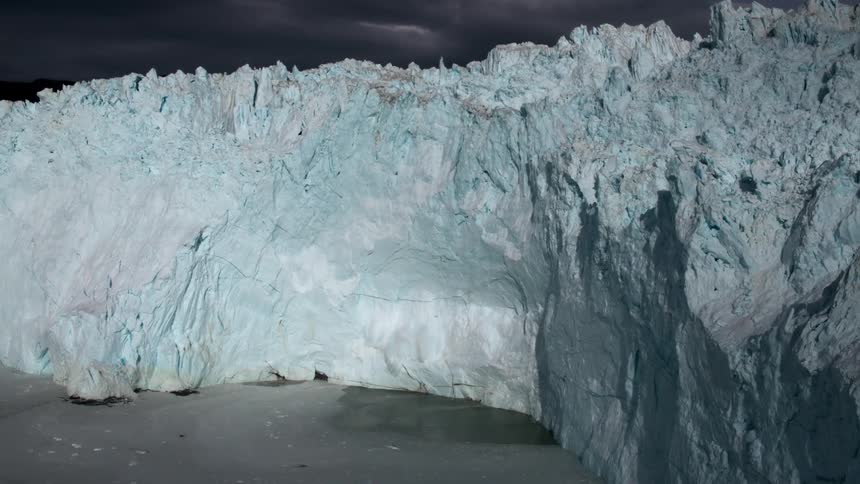 Snow and ice calves off a glacier and splashes in the ocean