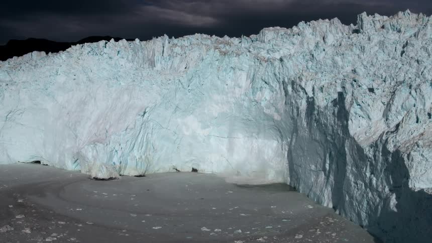 Snow and ice calves off a glacier and splashes in the ocean