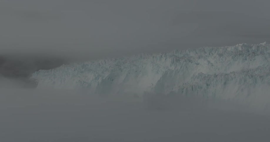 Fog and clouds drift over a glacier on a stormy day