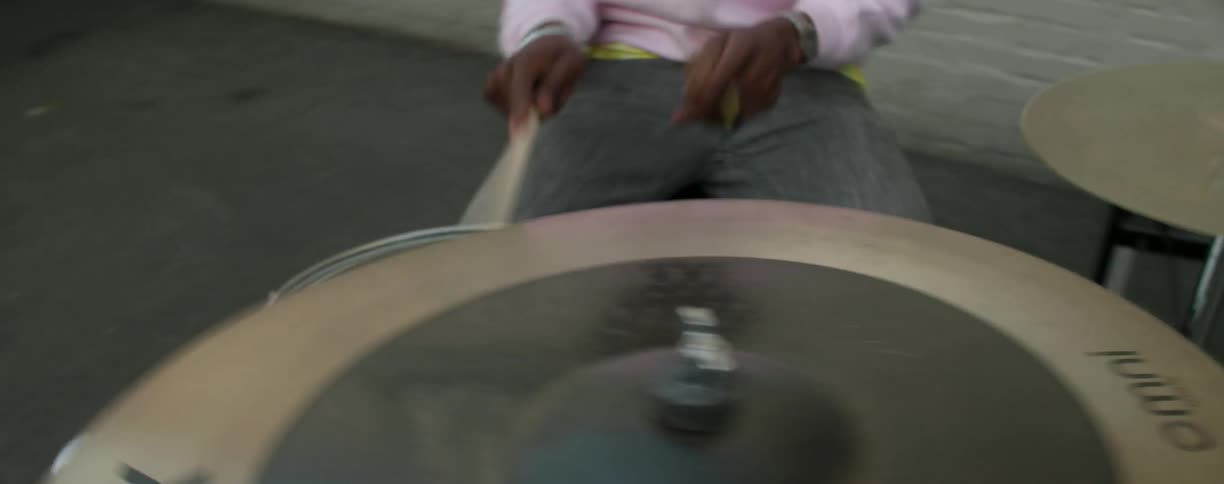 A man is playing the drums in a parking lot at dusk