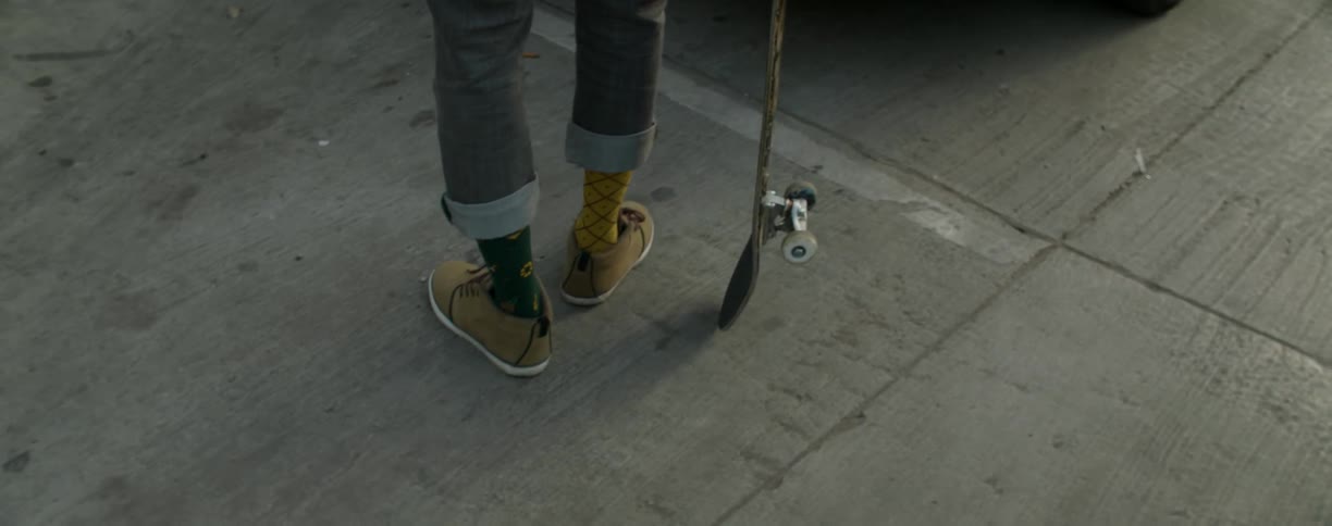 A man is shifting his stance as he stands in a parking lot holding a skateboard