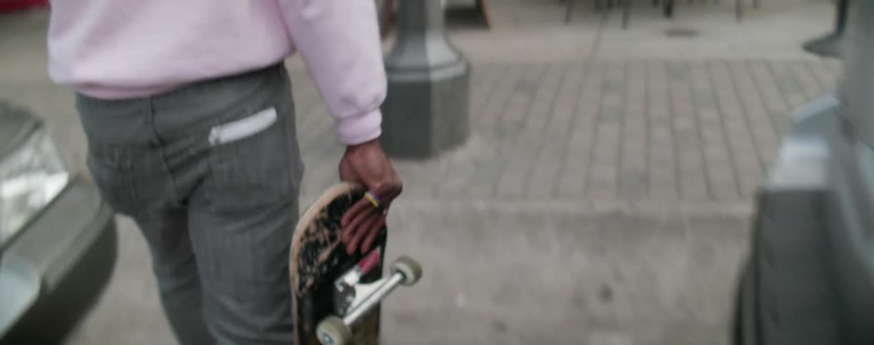 A man is carrying a skateboard as he walks into a shop in the city