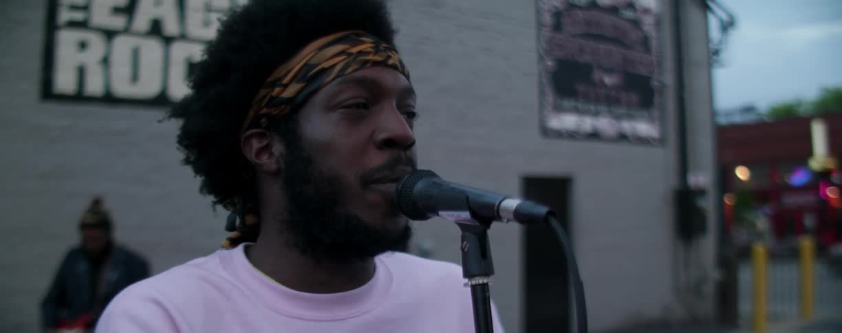 A man is standing on a street corner with a microphone addressing crowd