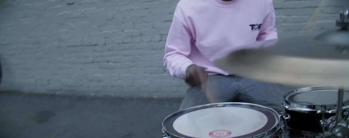 A man is playing drums while others are watching and walking around