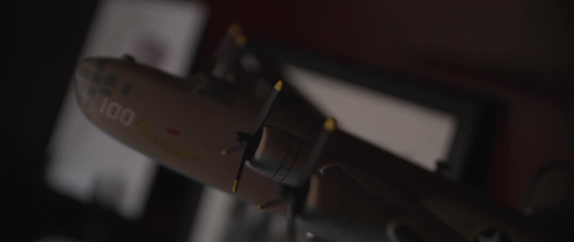 A close view of a model of a military plane on a shelf with framed photos in the background